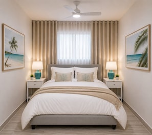 Een slaapkamer met een bed, twee nachtkastjes met lampen, een plafondventilator en twee ingelijste foto’s aan de muur.