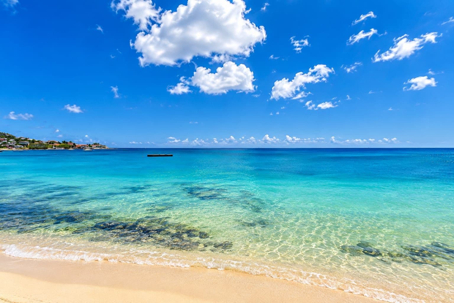 A beach with clear turquoise water, a sandy shore, and a distant boat.