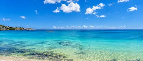 A beach with clear turquoise water, a sandy shore, and a distant boat.