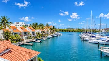 A marina with boats docked, a clear blue sky, and buildings with red-tiled roofs.