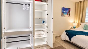 A hotel room with a wardrobe, a bed, a nightstand, a lamp, and a painting on the wall.