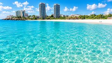 A beachfront hotel with clear turquoise water, a sandy beach, and high-rise buildings in the background.