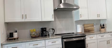 Une cuisine avec des armoires blanches, une hotte de cuisinière en acier inoxydable, une machine à café et un bloc à couteaux posé sur le plan de travail.