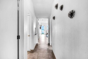 Un pasillo con paredes blancas, piso de baldosas y tres adornos negros en la pared.