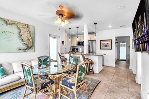 A modern kitchen with a microwave, refrigerator, and dining area with wicker chairs and a glass table. - Hollywood Beach | 3BR Steps to the Sand (Hollywood)