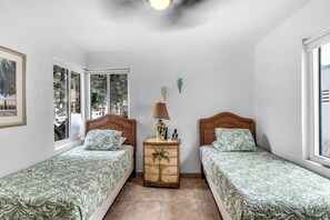 A bedroom with two single beds, a wooden nightstand, a lamp, and a window with a view of trees. - Hollywood Beach | 3BR Steps to the Sand (Hollywood)