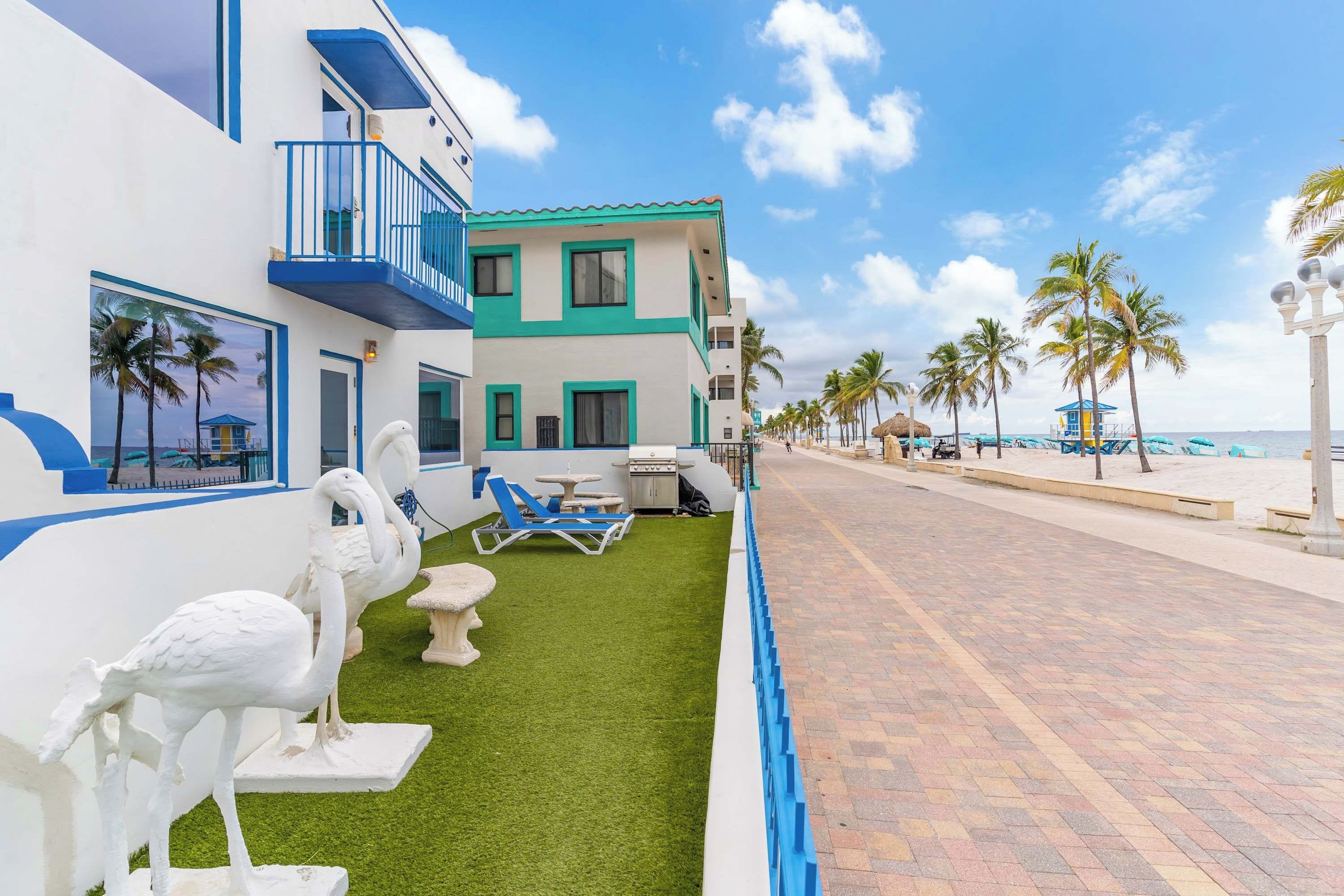 Un hotel frente a la playa con piscina, palmeras y cielo despejado.