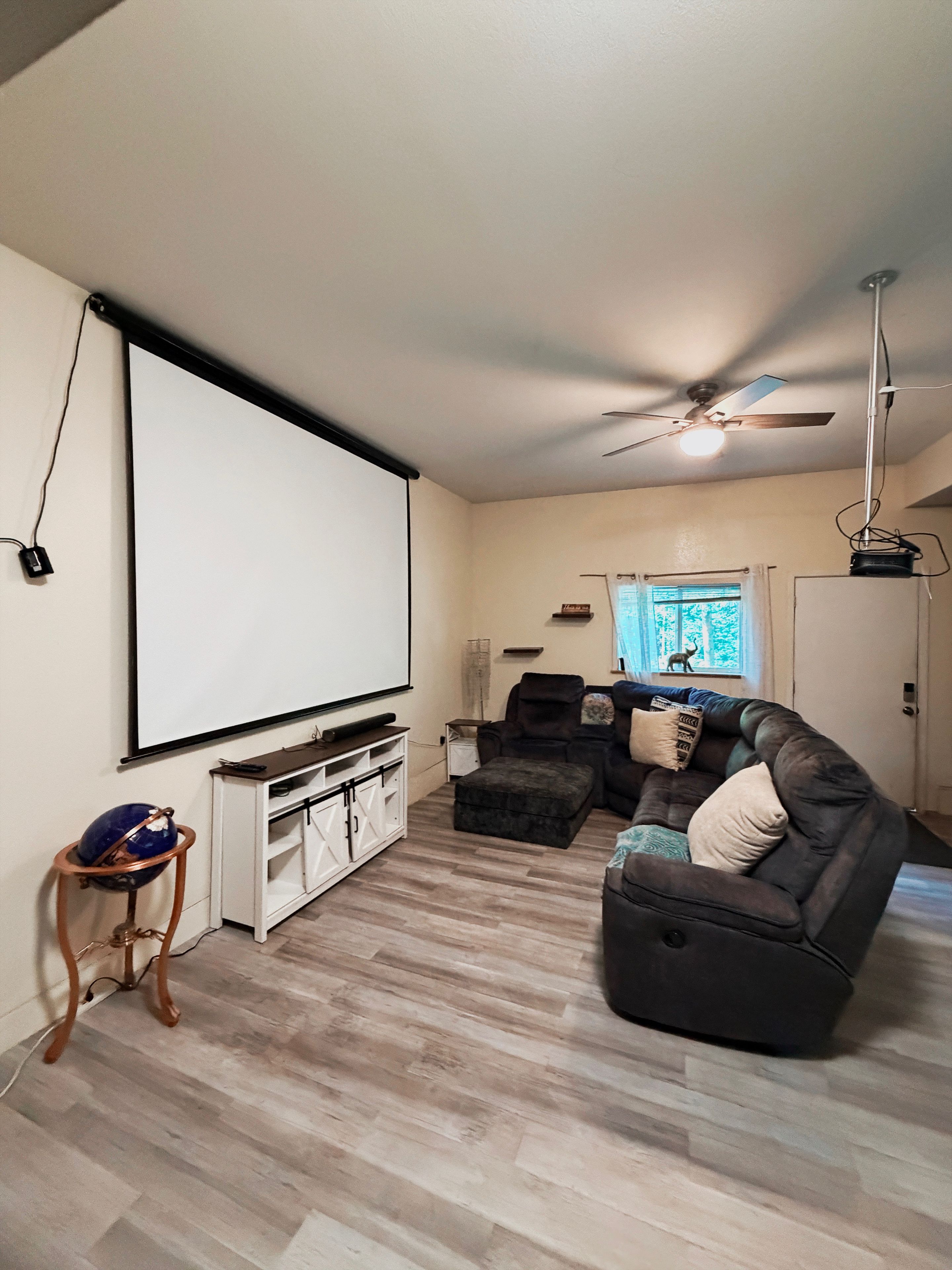 A living room with a large flat-screen TV, a ceiling fan, a sectional sofa, and a wooden floor.