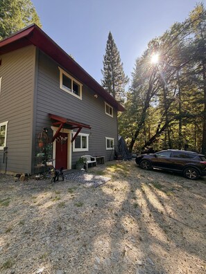 A two-story house with a red roof, a covered porch, and a car parked in the driveway. - Cross Creek Cabin - Private Redwoods, 2 Creeks, Massage Bed & 100" Theater (Redway)