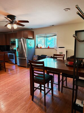 A kitchen with wooden cabinets, a stainless steel refrigerator, a dining table with chairs, and a ceiling fan.
