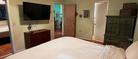 A bedroom with a bed, a ceiling fan, a television, a dresser, and a door.