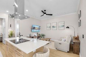 A modern kitchen with an island, a dining area with a sofa, and a flat-screen TV mounted on the wall. - Poolside Fun, Pickleball & Coastal Adventures Await in Fort Myers - Jefferson Palms I - Roelens (Fort Myers Beach)