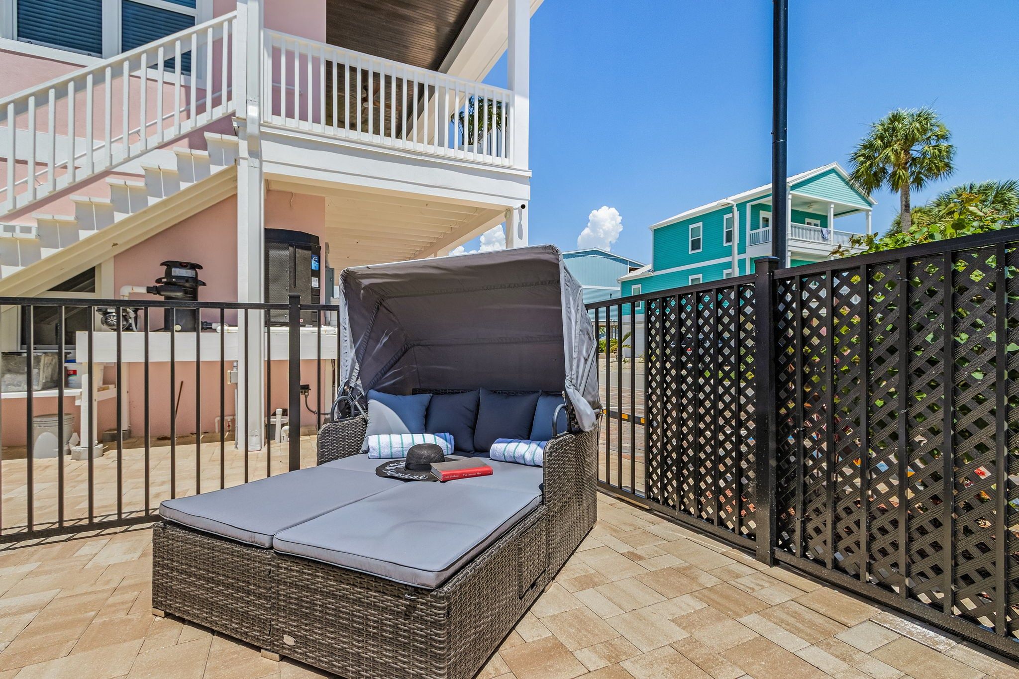 A covered outdoor seating area with a wicker sofa and cushions, a table with a book, and a view of a building with a balcony.