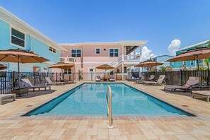 A swimming pool with lounge chairs and umbrellas, surrounded by a fence, with buildings in the background. - Poolside Fun, Pickleball & Coastal Adventures Await in Fort Myers - Jefferson Palms II - Roelens (Fort Myers Beach)