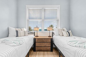 A bedroom with two beds, a wooden nightstand, and a window with blinds. - Poolside Fun, Pickleball & Coastal Adventures Await in Fort Myers - Jefferson Palms II - Roelens (Fort Myers Beach)