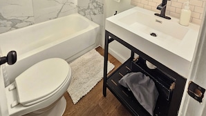 A bathroom with a white toilet, a bathtub, a sink with a mirror, and a towel rack.