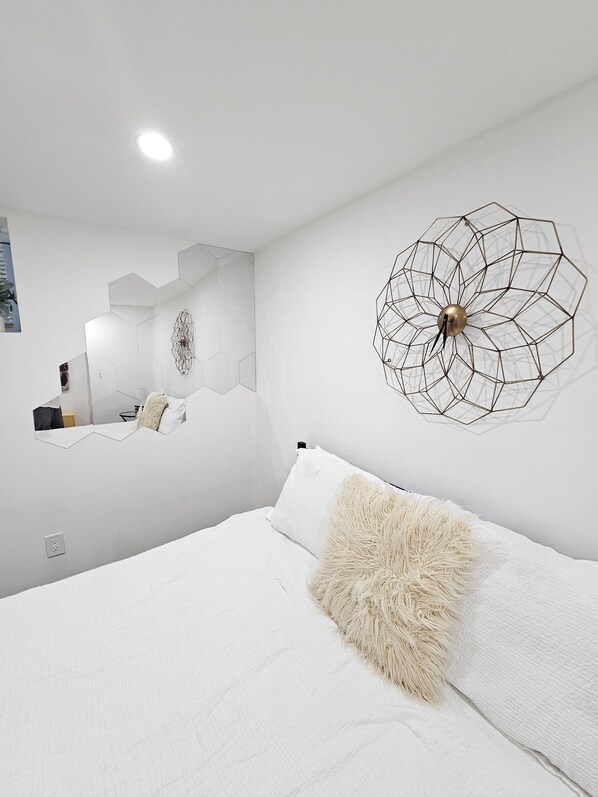 A modern bedroom with a large bed, a geometric wall decoration, and a mirror reflecting the room.