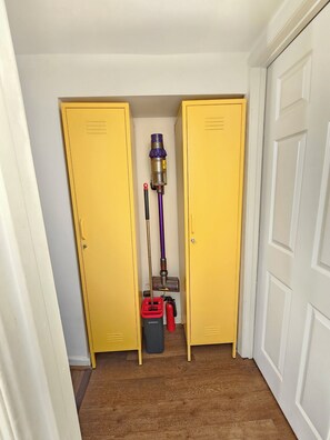 A hallway with two yellow lockers, a vacuum cleaner, and a red bucket.