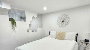A bedroom with a large bed, a wall-mounted geometric light fixture, and a small round table.