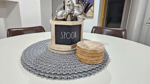 A dining table with a placemat, a wooden box labeled 'SPOON,' and stacked coasters.