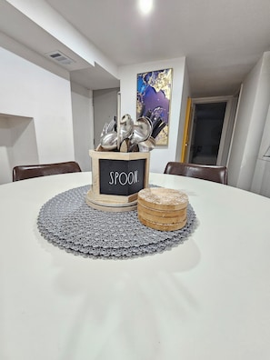 Una mesa de comedor con un mantel individual, una caja de madera con la etiqueta 'SPOON' y posavasos apilados.