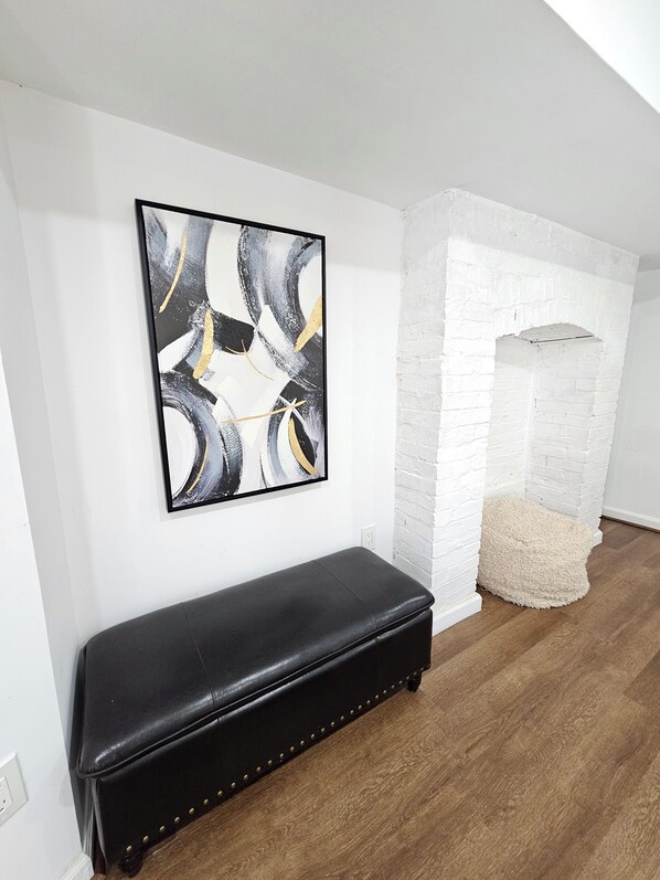 A room with a black leather bench, a white brick fireplace, and a large abstract painting on the wall.