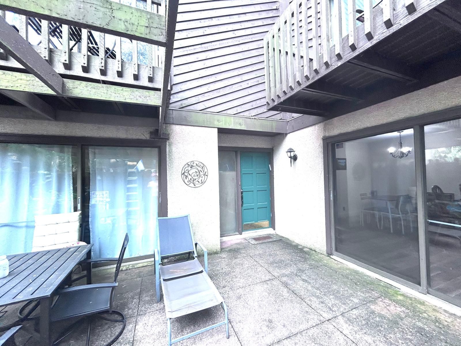 Un espace extérieur aménagé en terrasse, avec une table et des chaises, une porte bleue et un mur orné d’un motif circulaire.