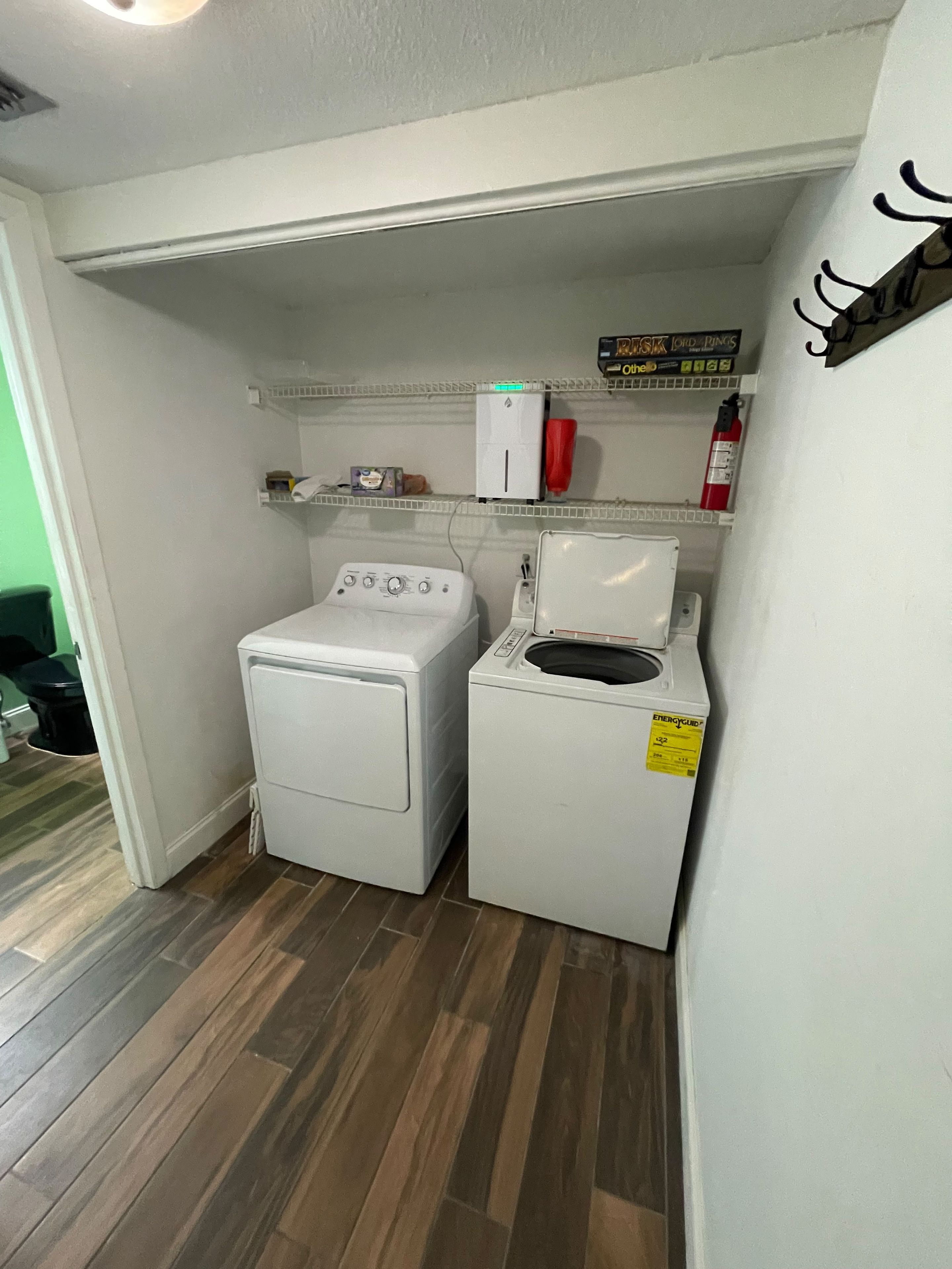 Een wasruimte met een wasmachine en droger, een plank met een brandblusser, en een klein plankje met een klok en een doos.