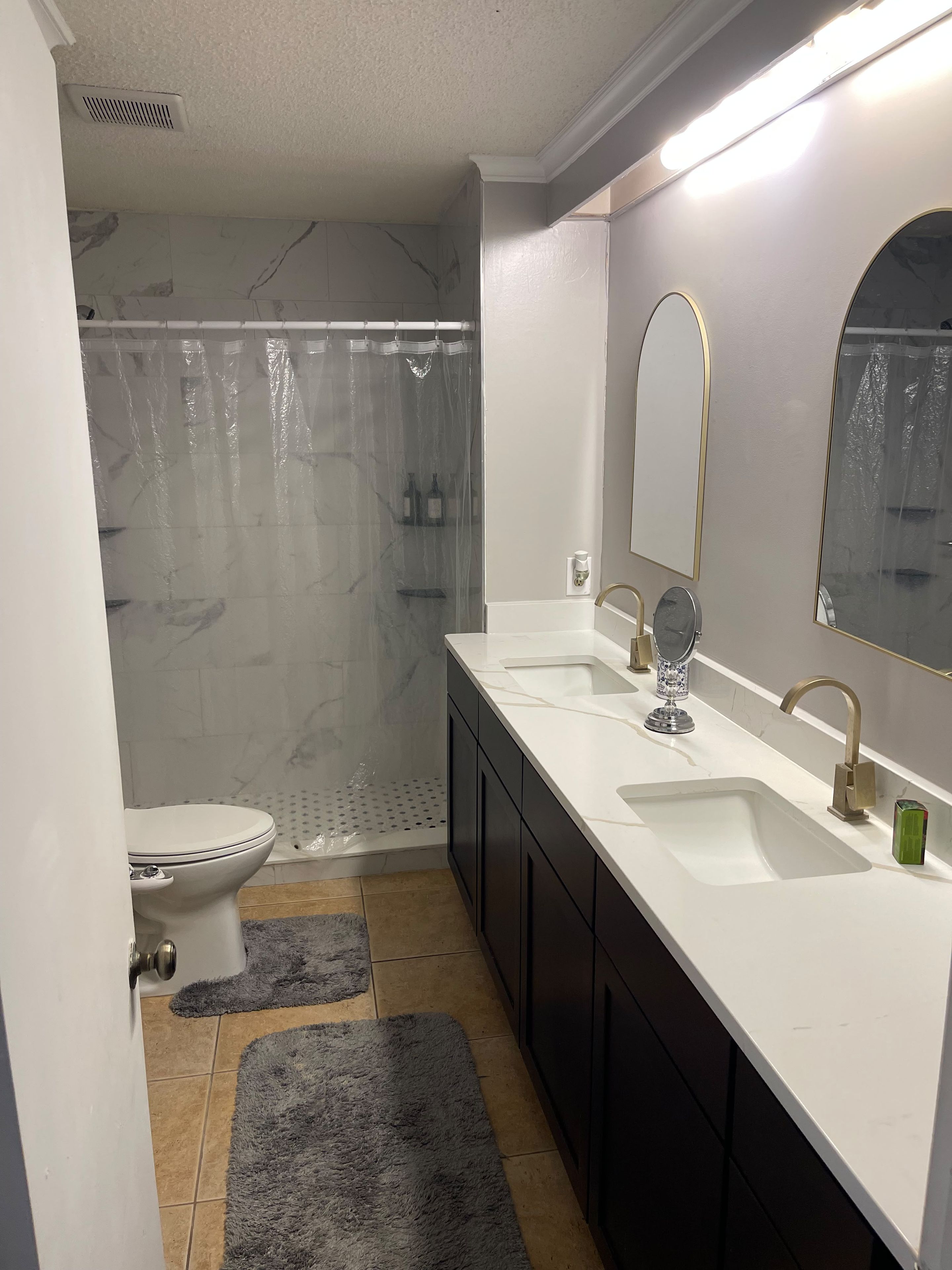 A bathroom with a toilet, a shower with a transparent curtain, a sink with a mirror, and a towel rack.