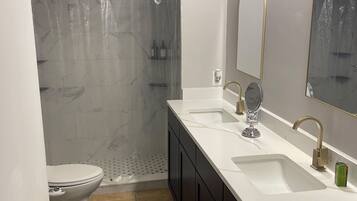 A bathroom with a toilet, a shower with a transparent curtain, a sink with a mirror, and a towel rack.