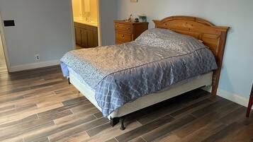 A bedroom with a bed, wooden headboard, nightstand, and a bathroom with a mirror and sink.