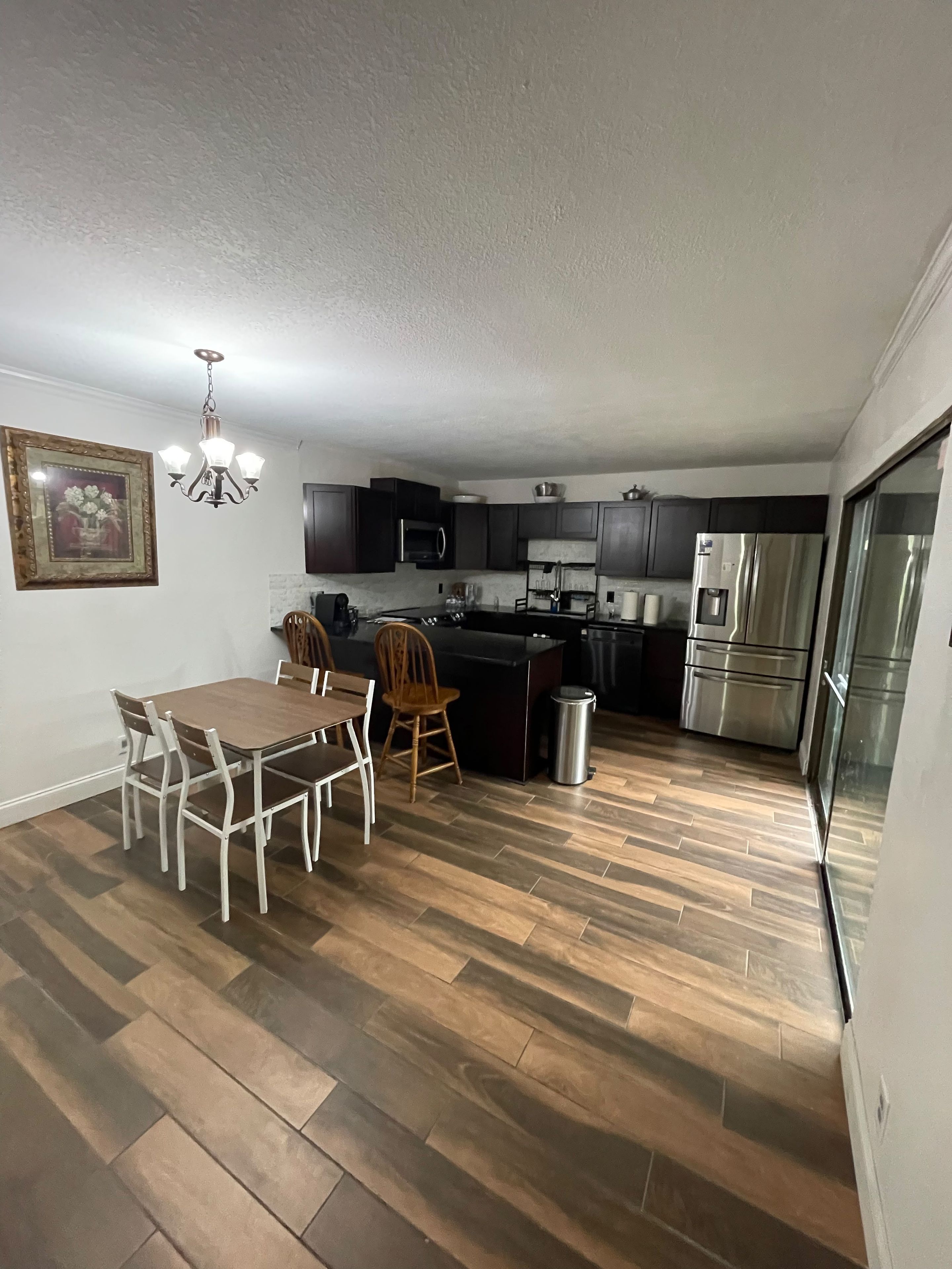 A modern kitchen with dark cabinets, a stainless steel refrigerator, a microwave, and a dining area with a table and chairs.