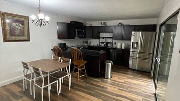 A modern kitchen with dark cabinets, a stainless steel refrigerator, a microwave, and a dining area with a table and chairs.