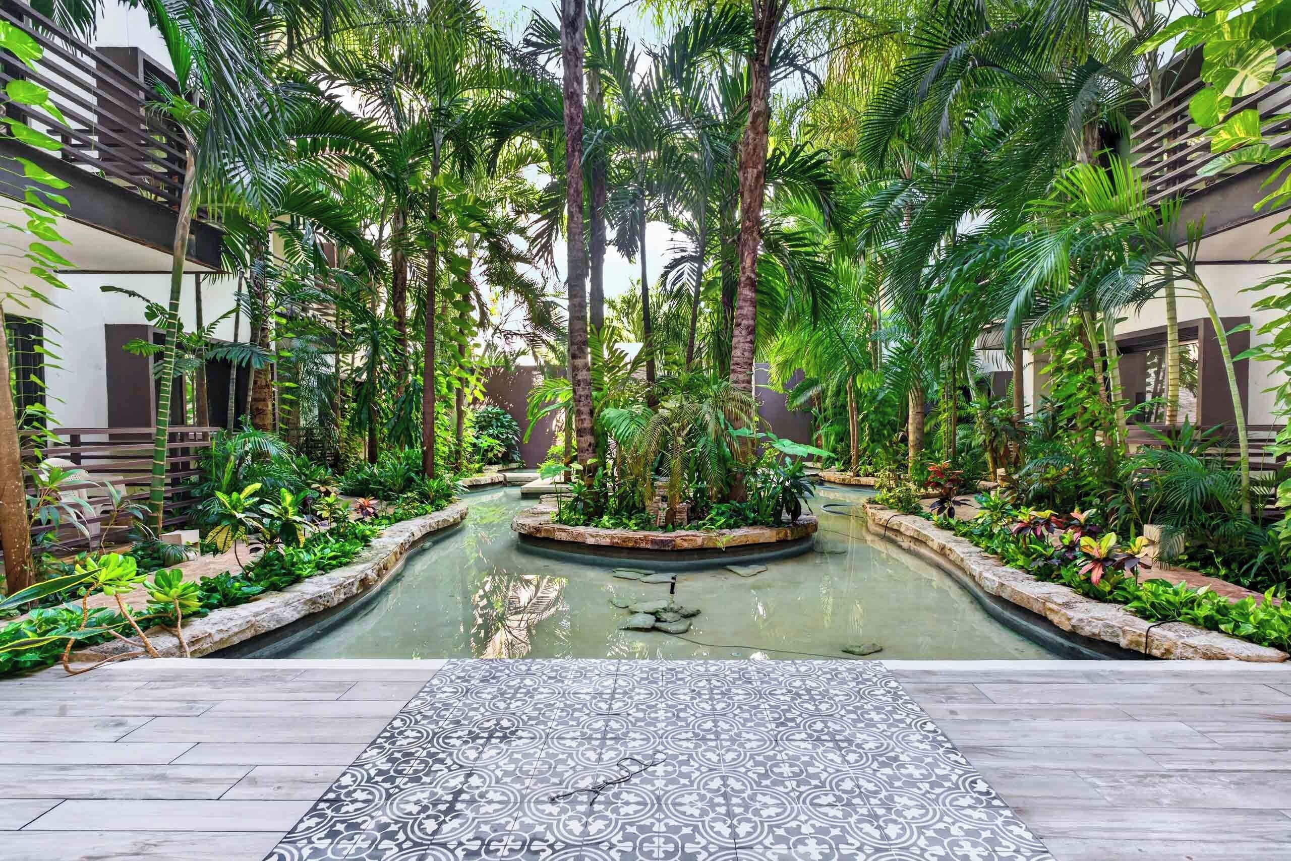 Un jardin intérieur paisible, avec une fontaine centrale, entouré d’une végétation luxuriante et doté d’un sol à motifs.