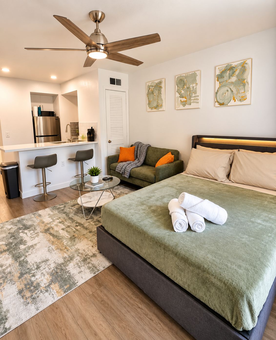 A modern bedroom with a bed, a ceiling fan, a kitchenette, and a dining area.