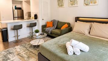 A modern bedroom with a bed, a ceiling fan, a kitchenette, and a dining area.