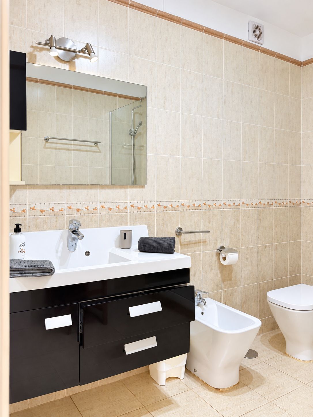 Un baño moderno con un lavamanos blanco, tocador negro y un bidé.