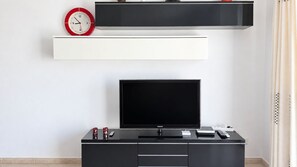 A modern living room with a flat-screen TV, a clock, and a coffee table with electronic devices. - Mareverde Sea View Apartment with Pool (Costa Adeje)