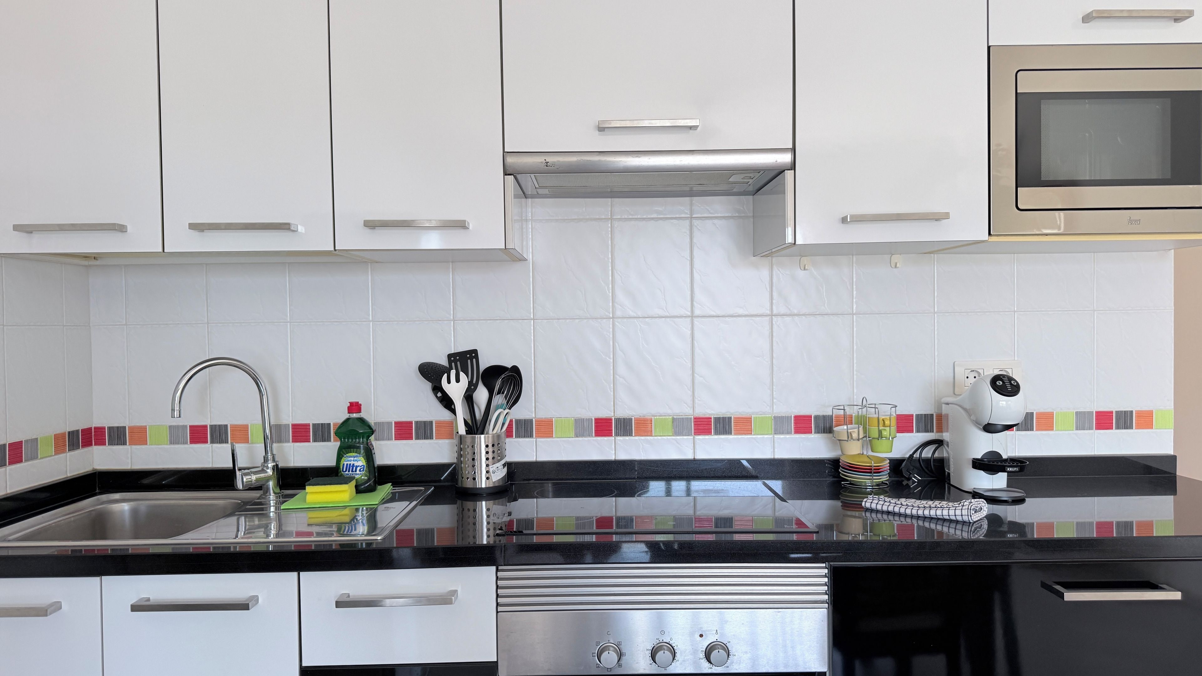 Cozinha moderna com armários brancos, fogão de aço inoxidável e micro-ondas.