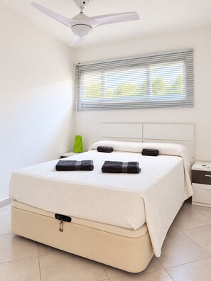 A neatly made bed with a white headboard, a ceiling fan, and a window with blinds. - Mareverde Sea View Apartment with Pool (Costa Adeje)