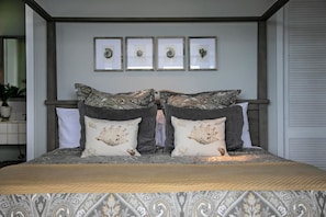 A bedroom with a bed, two decorative pillows, a headboard, and three framed pictures on the wall. - Romantic Getaway | Oceanfront | Private Pool (St. Thomas)