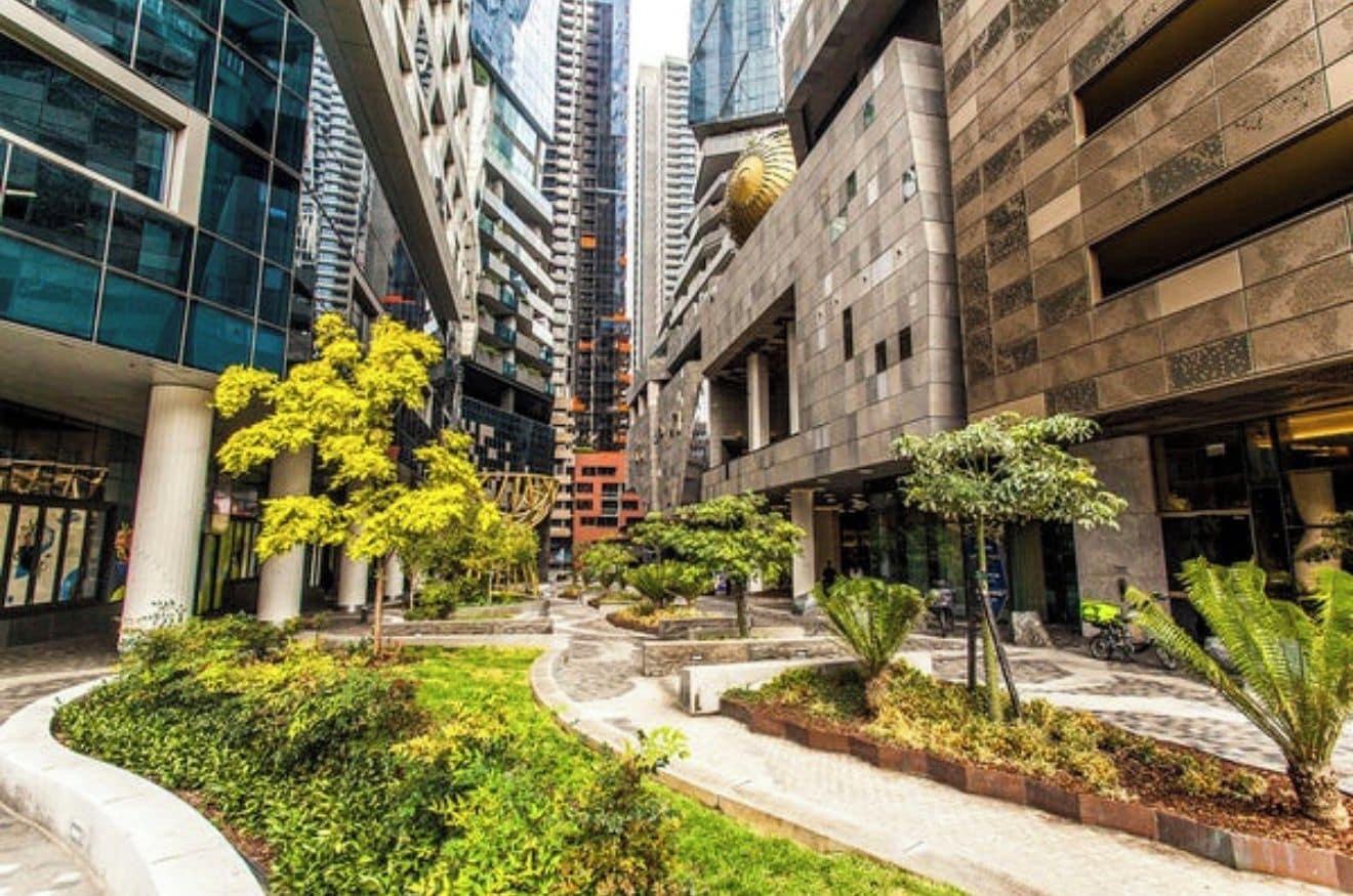 A modern urban plaza with high-rise buildings, landscaped gardens, and a central fountain.