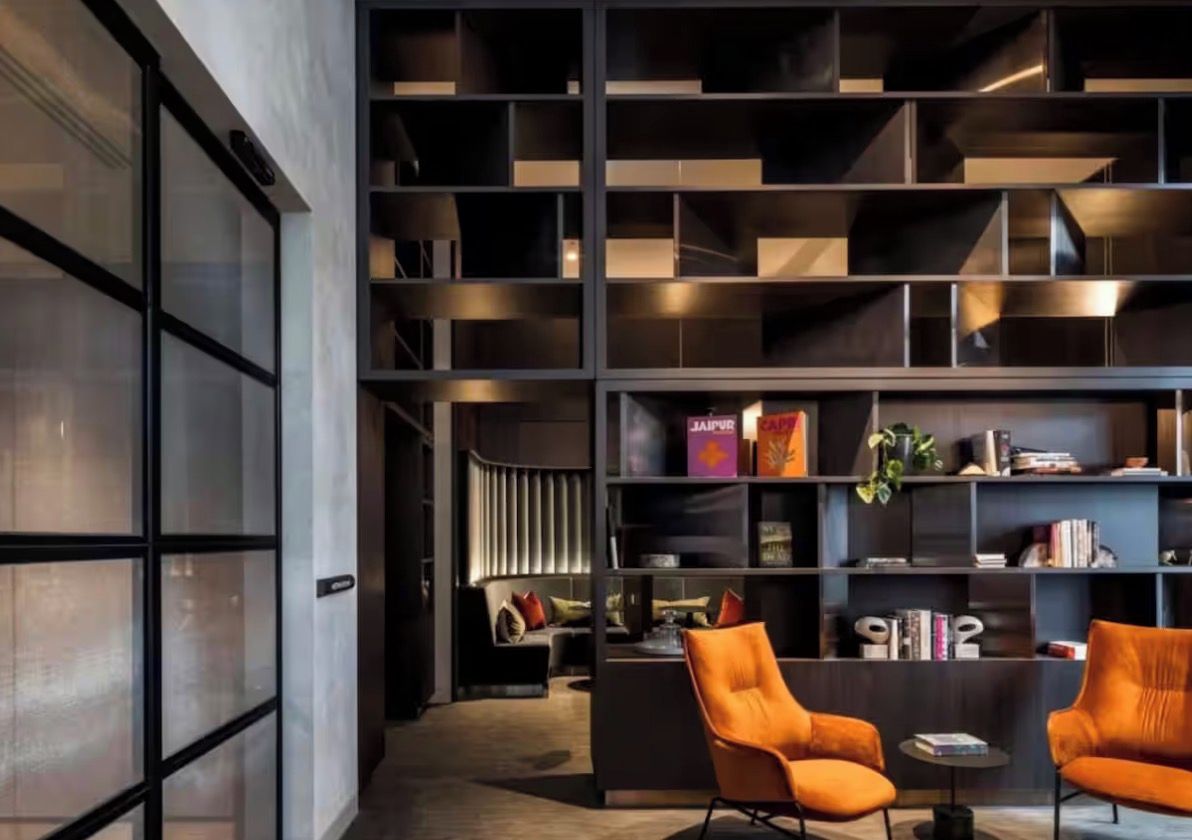 A modern interior with a large bookshelf, two orange chairs, and a small table.
