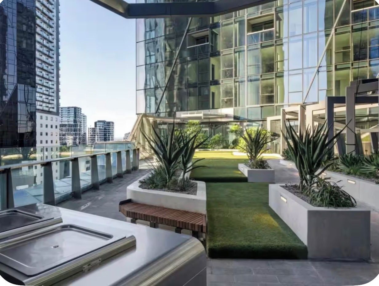 A modern rooftop terrace with a glass building, planters, and a pathway.