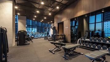 A gym with various exercise equipment, large windows, and a high ceiling.