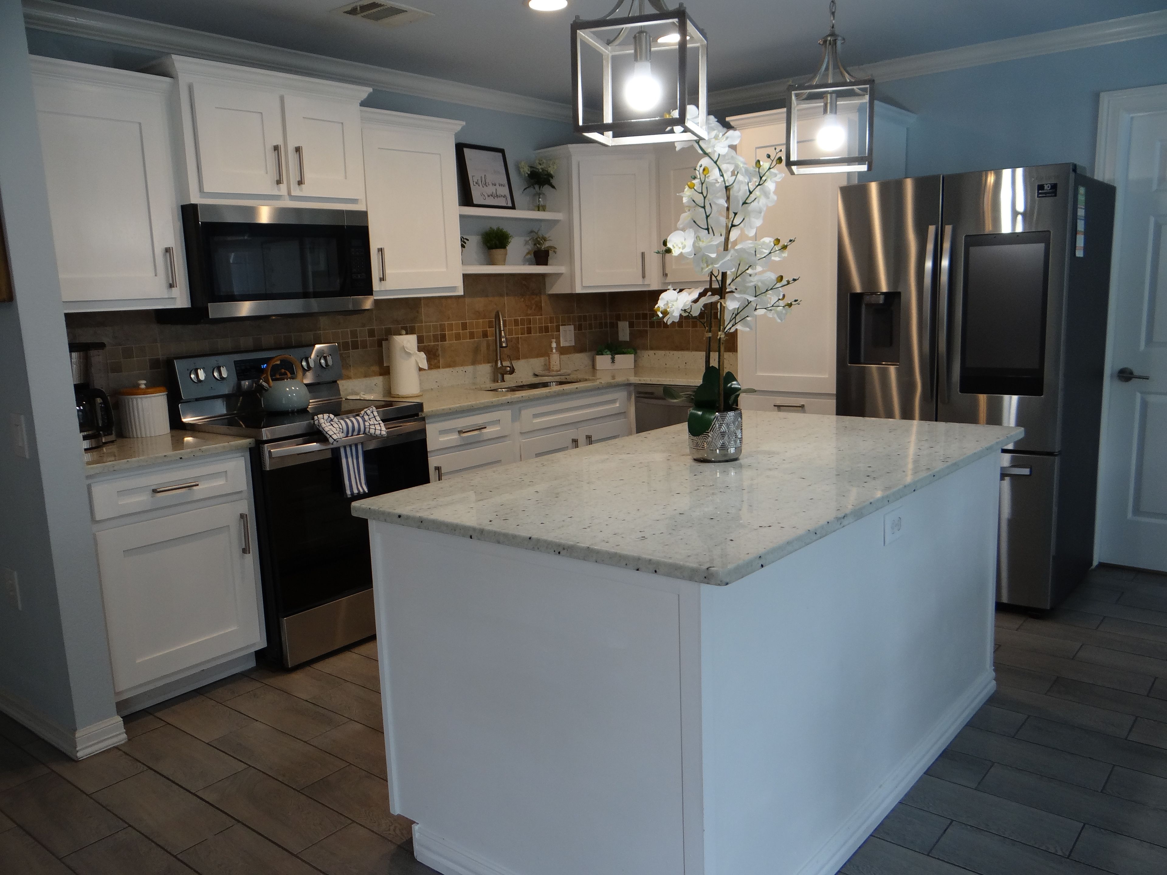 A modern kitchen with white cabinetry, stainless steel appliances, and a central island with a vase of flowers.