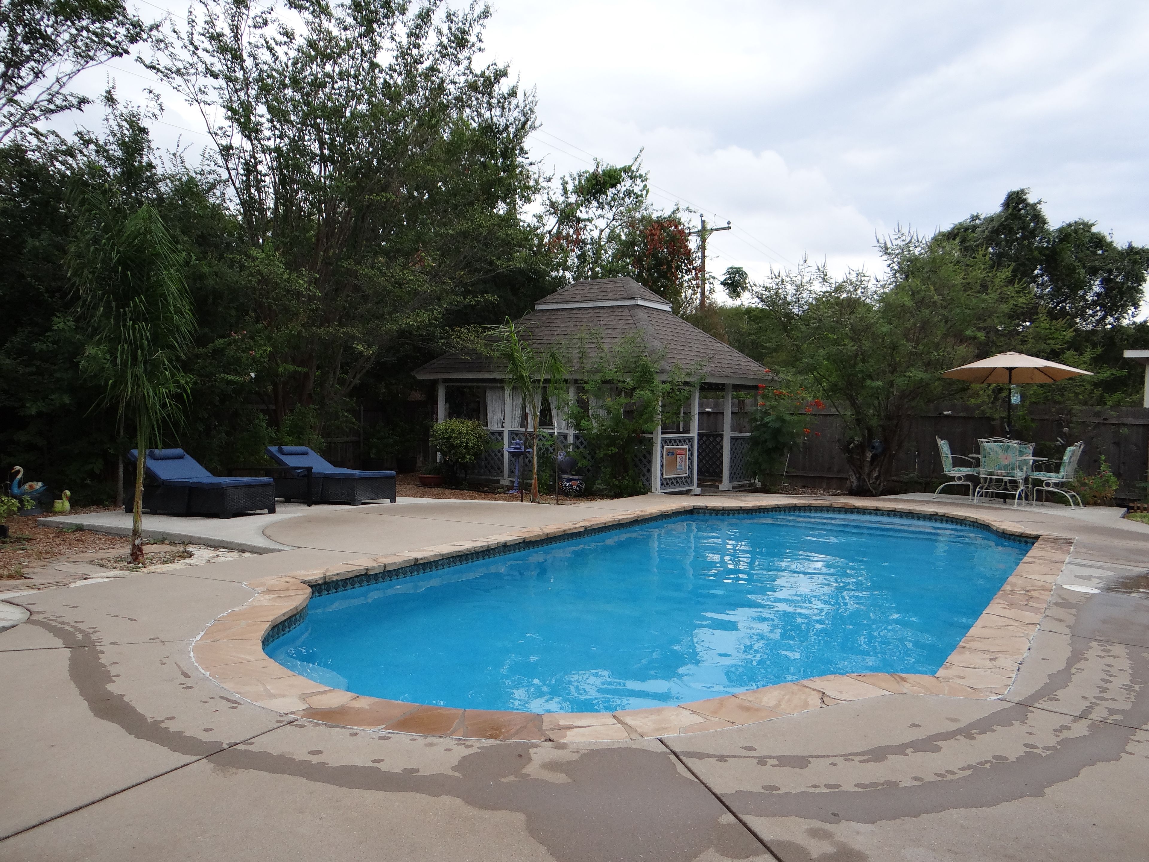 Un jardin avec une piscine, des chaises longues et un patio couvert.