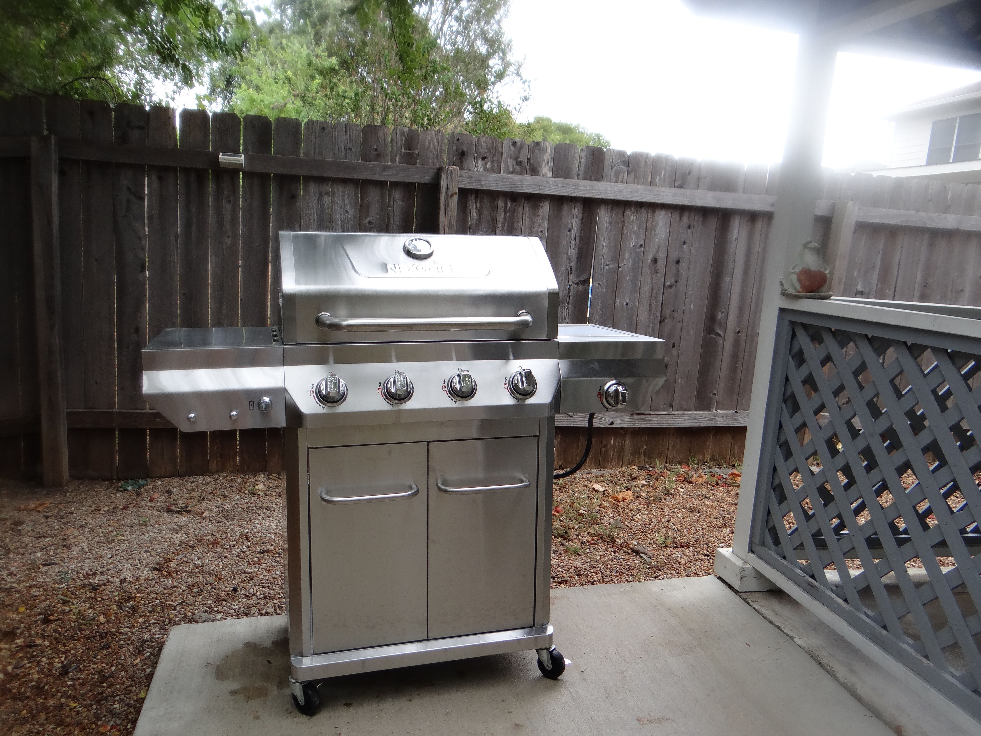 A stainless steel barbecue grill with four burners and a side burner, mounted on a wheeled cart.