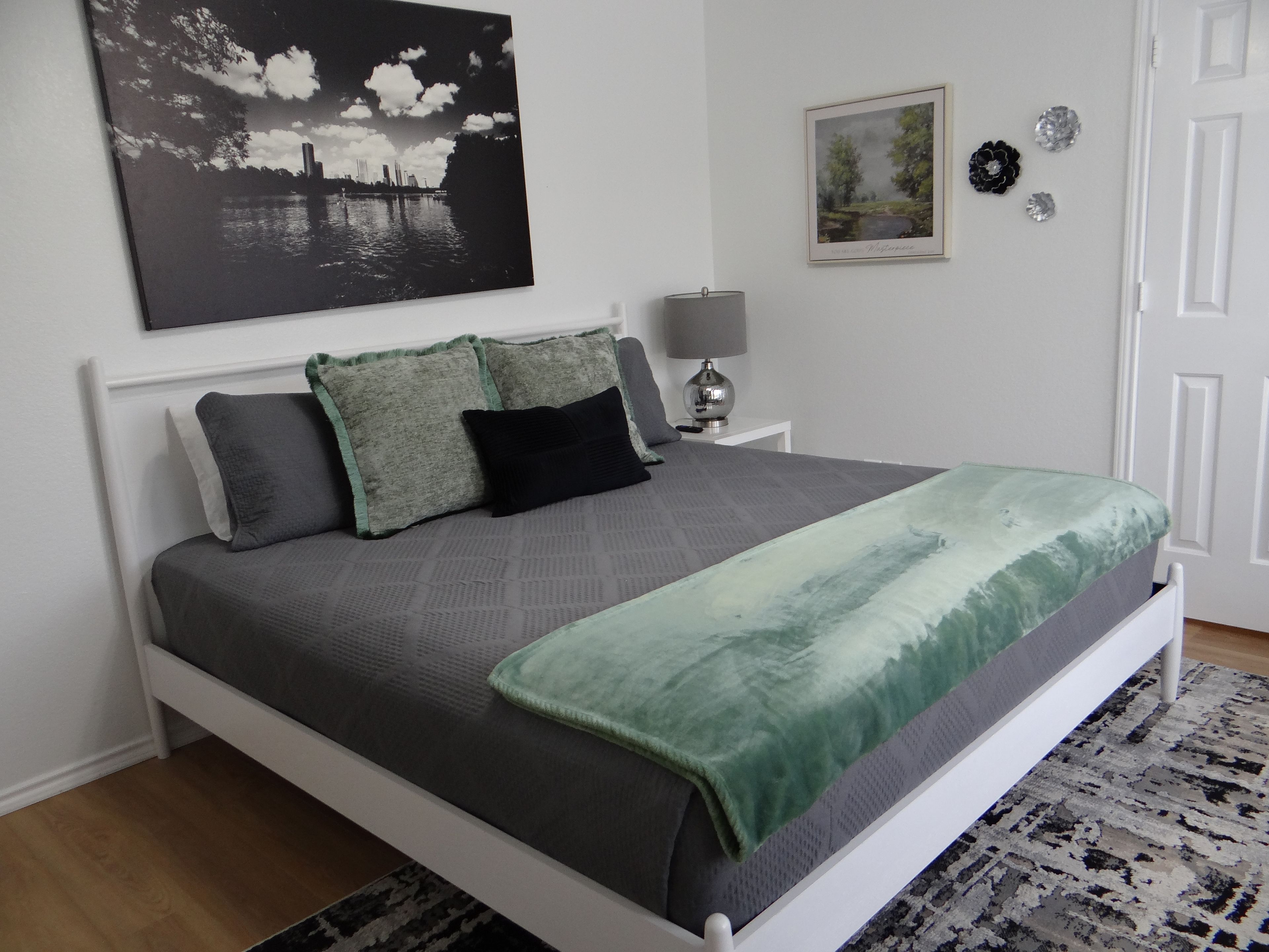 A bed with a grey and green blanket, a white headboard, and a grey pillow.