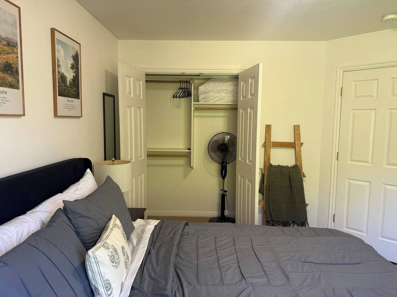Een slaapkamer met een bed, een ventilator, een houten trap en een kast met kledingroede.